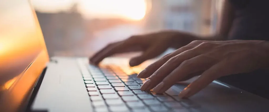 Mão feminina digitando em notebook, representando a criação de conteúdo slow content.