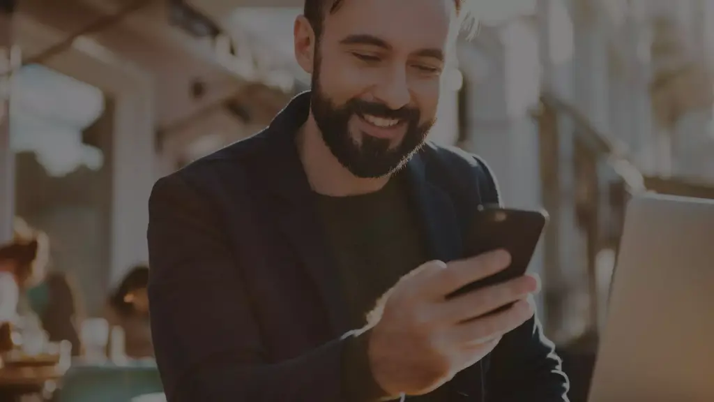 Homem sorrindo para a tela do celular, simbolizando a hiperpersonalização na jornada de compra.