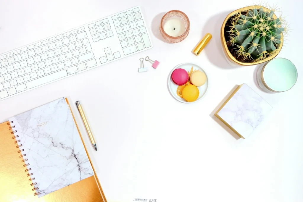 Mesa de trabalho organizada com teclado, caderno, caneta, vela, cacto e macarons.
Foto de mesa de trabalho com itens de escritório e decoração.
Imagem de mesa de trabalho com teclado, caderno e outros objetos.